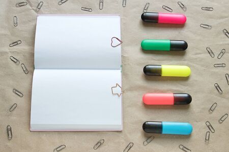 Opened notebook with shaped paper clips on pages and colored highlighters surrounded by paper clipsの写真素材