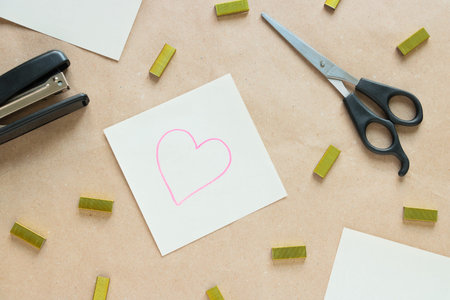 A pair of cissors, stapler, staples and a sticky note with a picture of a heart