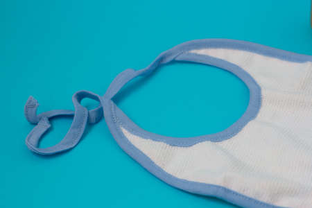 Baby white bib on blue background. Kids cloth for feeding. Child clothing during meal time. Newborn accessories.の写真素材