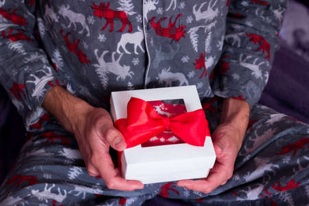 Christmas loneliness. Man in comfy pajamas opening present. Quarantine Holiday celebration. New Year gift deliveryの写真素材