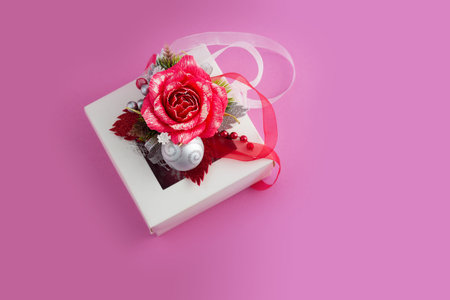 Christmas card with copy space for text. Top view of White gift box with red rose and bauble on pink...