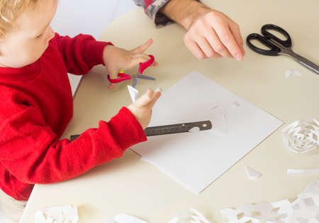Cute little Boy cuts out snowflakes for Christmas decoration. New Year Decor. Festive craft and seasonal activityの写真素材