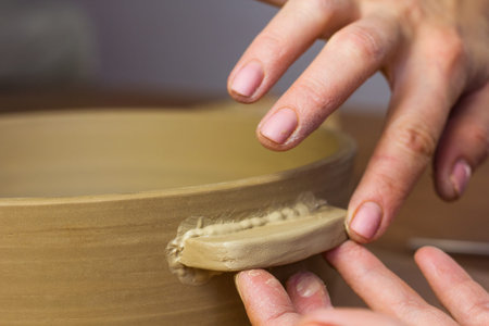Woman ceramist attaching handle to the pot in pottery class. Potter workshop in ceramic studio