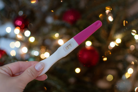 Hand holding positive pregnancy test on a Christmas tree background.の写真素材