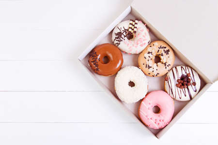 Colored delicious donuts with sprinkles in a box on a white wooden backgroundの写真素材