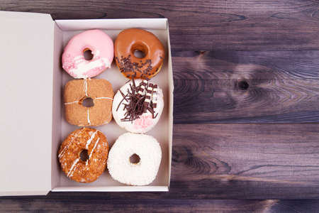 Colorful delicious donuts with glaze and sprinkles in a box on a dark wooden table. Top view with copy spaceの写真素材