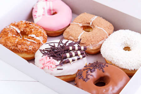 Colorful delicious donuts with chocolate and other sprinkles in a box on a wooden backgroundの写真素材