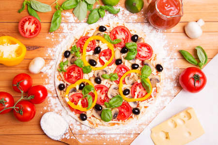 Prepared Italian pizza with sause, tomato and other ingredients other on the wooden backgroundの写真素材