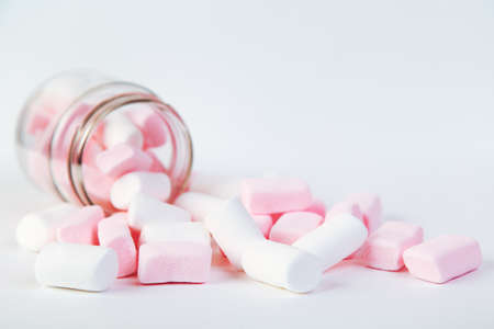 White and pink marshmallows spill out of the glass on the white backgroundの写真素材