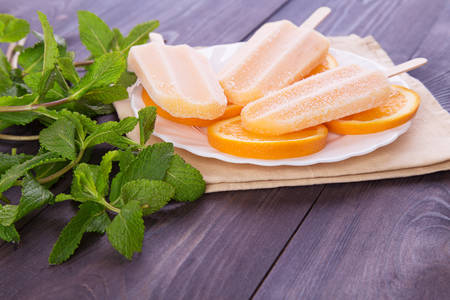Homemade frosty ice sticks on a plate with mint and orange slice on a dark wooden backgroundの写真素材