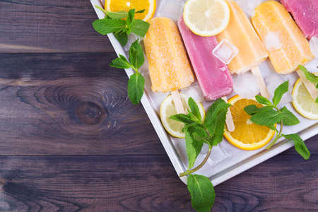 Frosty strawberry and orange ice cream ice sticks in a row on a steel tray with mint and ice.の写真素材