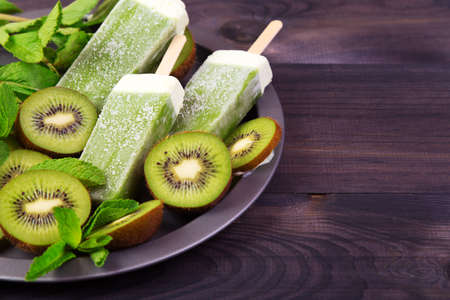 Homemade kiwi ice sticks on a plate with mint and kiwi slices on a dark wooden backgroundの写真素材