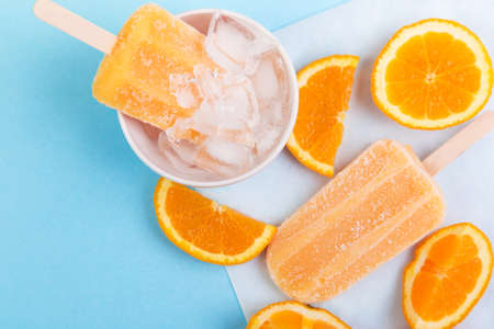 Homemade frosty orange ice sticks with orange slices and ice on a paper and blue background. Top view with copyspaceの写真素材