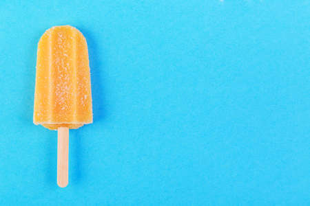 Single orange ice stick on a blue background. Top view with copyspaceの写真素材