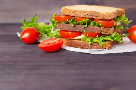 Sandwich with egg, salad and tomatoes on crispy slice of rye bread on a dark wooden background. Space for textの写真素材