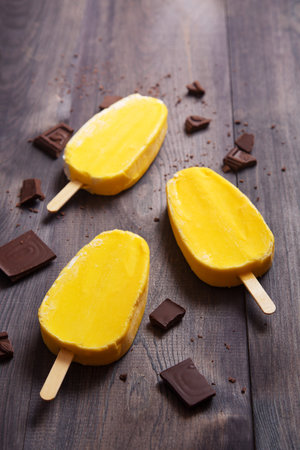 Yellow ice cream with chocolate bars on dark wooden background. Space for text.