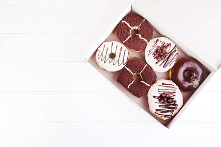 Colorful delicious donuts with sprinkles and glaze in a box on a white wooden background. Top view with copyspaceの写真素材