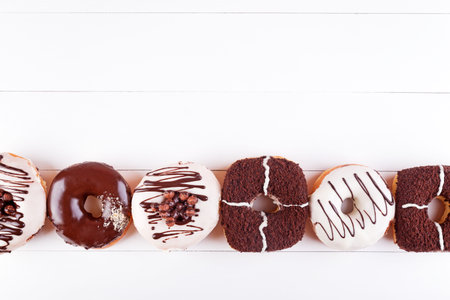 Colorful delicious donuts with chocolate, sweet glaze and sprinkles in a row on a white wooden background. Top view with copyspaceの写真素材