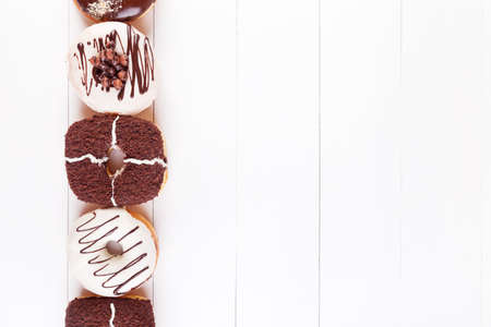 Sweet delicious donuts with chocolate, sweet glaze and sprinkles in a row on a white wooden background. Top view with copyspaceの写真素材