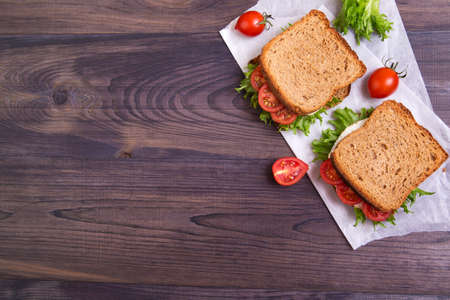Homemade sandwich with egg, salad and tomatoes on crispy slice of rye bread on a dark wooden background. Top view with copyspaceの写真素材