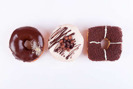 Colorful delicious donuts with chocolate, sweet glaze and sprinkles in a row on a white background. Top view with copyspaceの写真素材