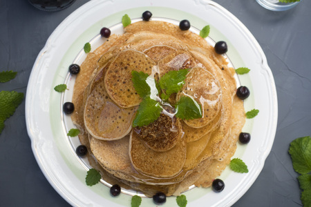 Pancakes are located in a plate on a gray background, decorated with berries and mint leaves. Pancakes in maple syrup.の写真素材