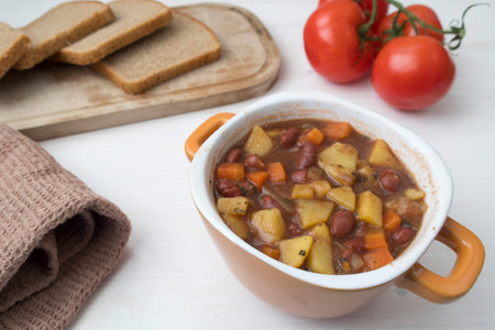 Appetizing beautiful soup with potatoes, onions, carrots and beans. Tomatoes and bread in the background. On a light background.の写真素材