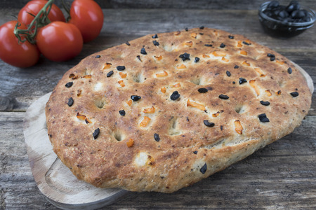 Traditional Italian focaccia homemade bread with tomatoes and black olives, on a wooden background close-up.の写真素材