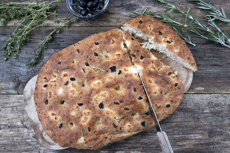 Traditional Italian focaccia homemade bread and a piece cut from it with tomatoes and olives, thyme and rosemary on a close-up wooden background.の写真素材