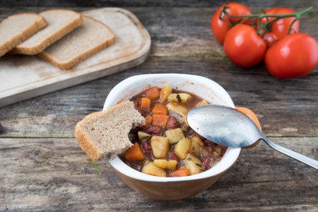 Appetizing beautiful soup with potatoes, onions, carrots and beans. On an old wooden background and close-up.の写真素材