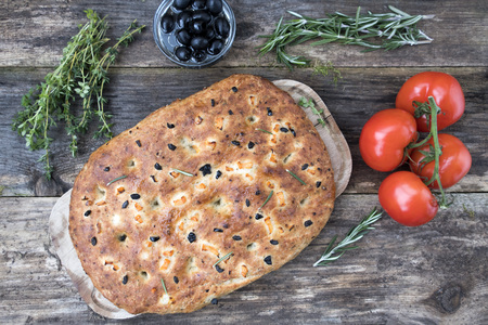Traditional Italian focaccia homemade bread with tomatoes and olives, thyme and rosemary on a close-up wooden background.の写真素材