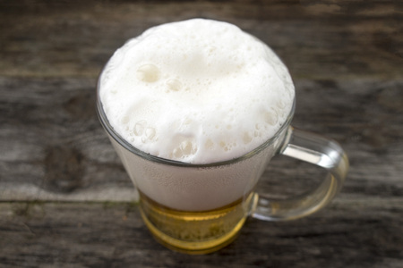Mug with a frothy beer close-up on a wooden background.の写真素材