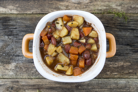 Appetizing beautiful soup with potatoes, onions, carrots and beans. On an old wooden background and close-up. View from above.の写真素材