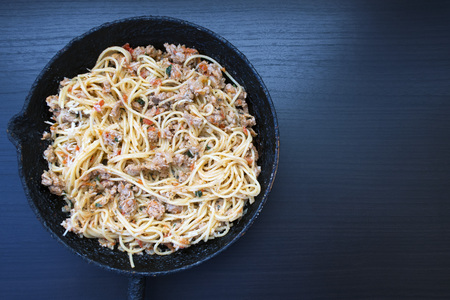 Appetizing spaghetti in an old frying pan with Bolognese sauce on a dark background close up and copy spaceの写真素材