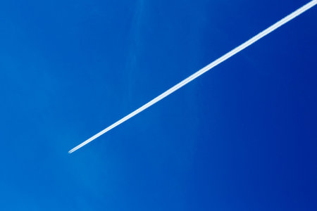 The plane flies high in the sky and the white track from the airplane