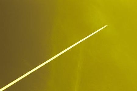 The plane flies high in the yellow sky and the white track from the airplaneの写真素材