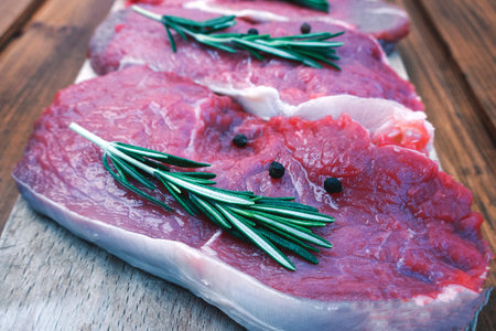 Raw pork steak with black pepper peas and rosemary on a wooden background close-up