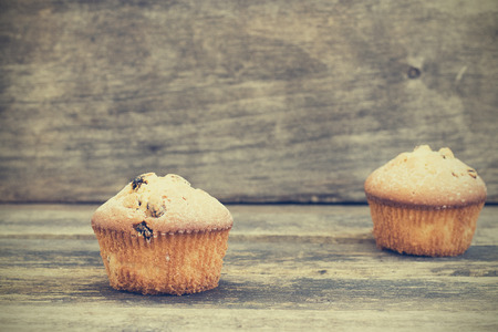 Two muffins with raisins sprinkled with powdered sugar on a wooden backgroundの写真素材