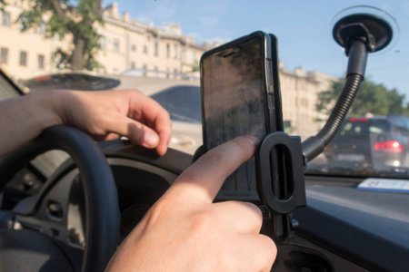 The driver looks at the route in the mobile phone which is fixed on the windshield and is located on...
