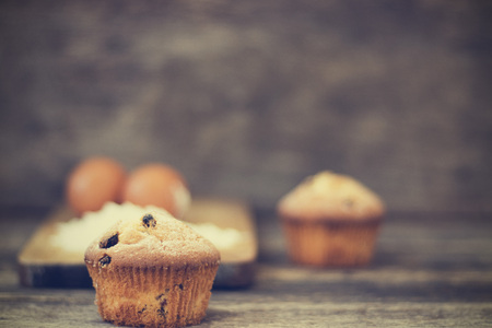 Muffin with raisins sprinkled with powdered sugar on a wooden background and are ingridient on the back of a blurry backgroundの写真素材