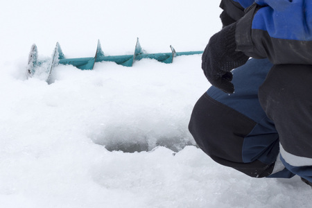 Winter, the fisherman bent over the fishing hole, the concept of winter fishing.の写真素材