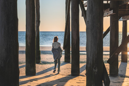 young woman running on the beach in front of a wooden pier.の写真素材