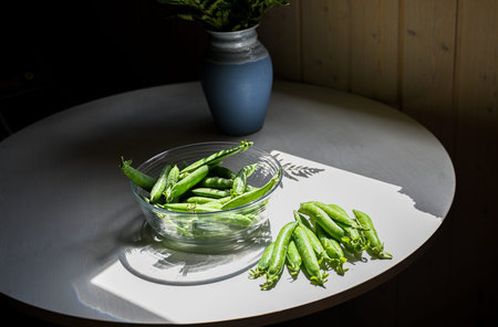 Fresh green peas in a glass bowl on a white wooden table.