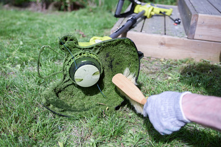 man cleaning a electric trimmer from grass after work with a brush, gardening concept