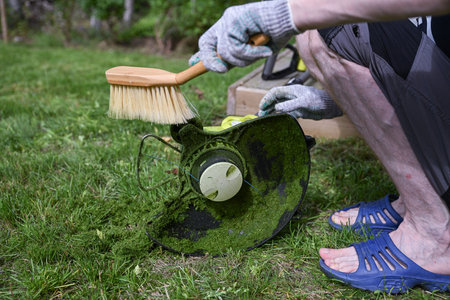 man cleaning a electric trimmer from grass after work with a brush, gardening concept