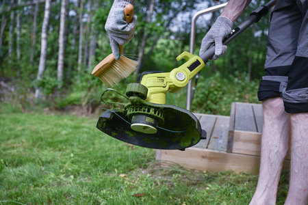man cleaning a electric trimmer from grass after work with a brush, gardening concept