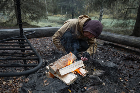 man starting a bonfire at picnic campfire in the forest