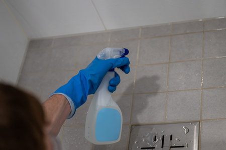 Man's hand in blue rubber gloves holding a spray bottle with detergent. Tile floor was partially washedの写真素材