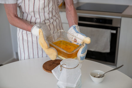 human hands pour melted butter into a glass jar through gauze. Cooking ghee oil