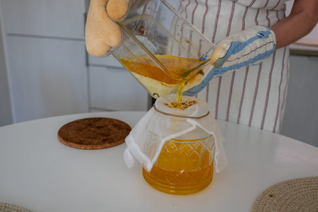 human hands pour melted butter into a glass jar through gauze. Cooking ghee oil
